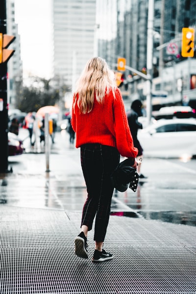 The woman is wearing a red sweater and black trousers
